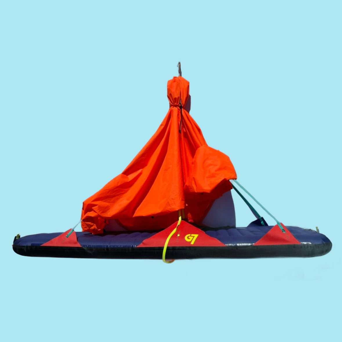 A red and blue portaledge climbing accessory with a waterproof cover on top, displayed against a clear blue sky.