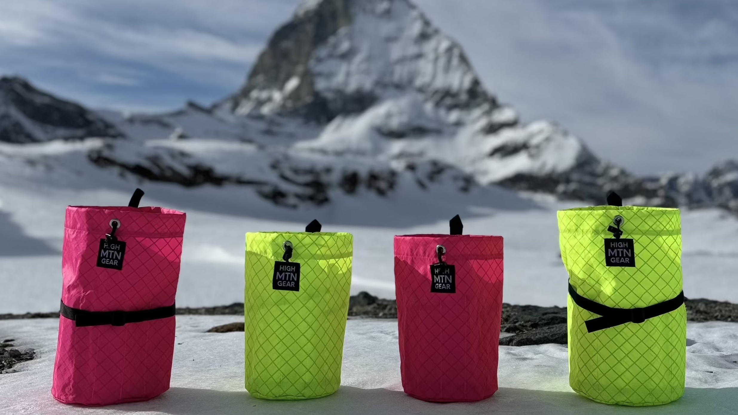 Four colorful bags on a snowy ground with a mountain in the background